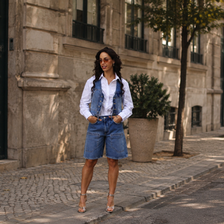 Mulher com look de transição verão-outono numa rua do Porto. Camisa branca, colete e calções de ganga e saltos altos dourados.